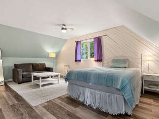 Discover this charming attic bedroom featuring a cozy seating area with a plush sofa and a modern coffee table, perfect for relaxation.