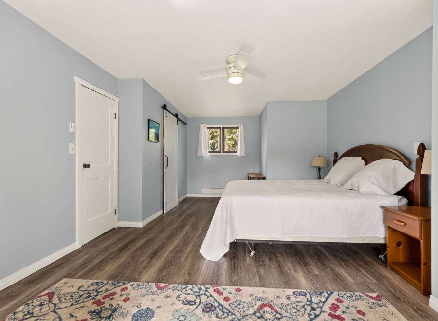 This charming bedroom features a comfortable queen-size bed with a white quilted comforter, complemented by a wooden headboard and matching nightstand.