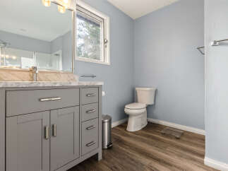 This modern bathroom features a sleek grey vanity with marble countertops, complemented by a large mirror and bright vanity lighting.