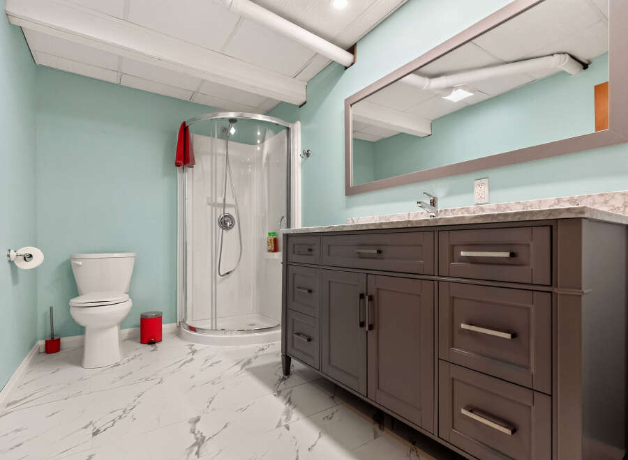 This modern bathroom features a sleek dark gray vanity with ample storage and a marble countertop, complemented by a spacious walk-in shower with a curved glass door.