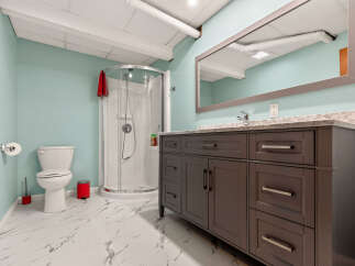 This modern bathroom features a sleek dark gray vanity with ample storage and a marble countertop, complemented by a spacious walk-in shower with a curved glass door.