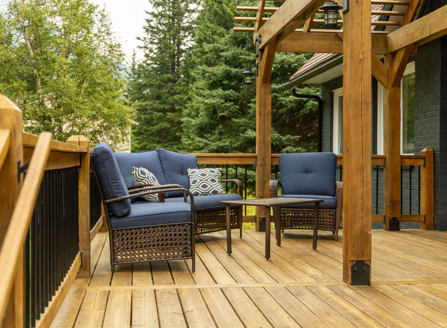 Enjoy outdoor living on this spacious wooden deck, complete with comfortable blue upholstered seating and a charming wicker coffee table.