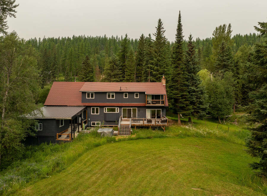 Nestled amidst a lush forest, this expansive home offers a serene retreat with its dark siding and warm red roof.