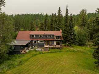 Nestled amidst a lush forest, this expansive home offers a serene retreat with its dark siding and warm red roof.