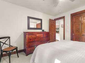 This charming bedroom features a spacious wooden dresser with a mirror, a comfortable bed with white quilted bedding, and a classic black chair with a woven seat.