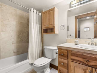 This charming bathroom features a bathtub with a travertine tile surround and a white shower curtain.