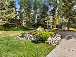 Discover a beautifully landscaped yard featuring a vibrant flower bed with colorful blooms and lush greenery, bordered by natural river stones.