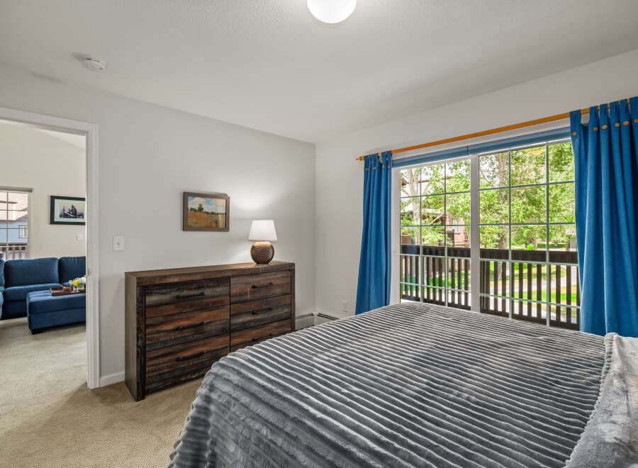 Experience comfort and style in this inviting bedroom, featuring a plush grey comforter on a spacious bed and a rustic wooden dresser.