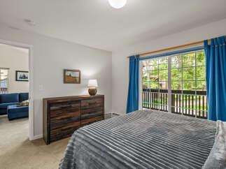 Experience comfort and style in this inviting bedroom, featuring a plush grey comforter on a spacious bed and a rustic wooden dresser.