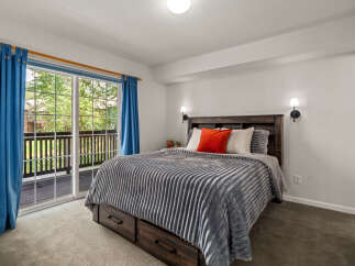 This inviting bedroom features a spacious bed with a plush grey comforter and decorative pillows, including a vibrant orange accent pillow.