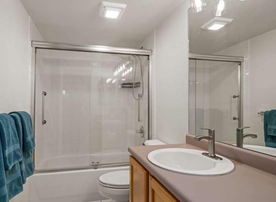 This bright and clean bathroom features a spacious bathtub with a sliding glass shower door and white tiled walls.