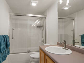 This bright and clean bathroom features a spacious bathtub with a sliding glass shower door and white tiled walls.