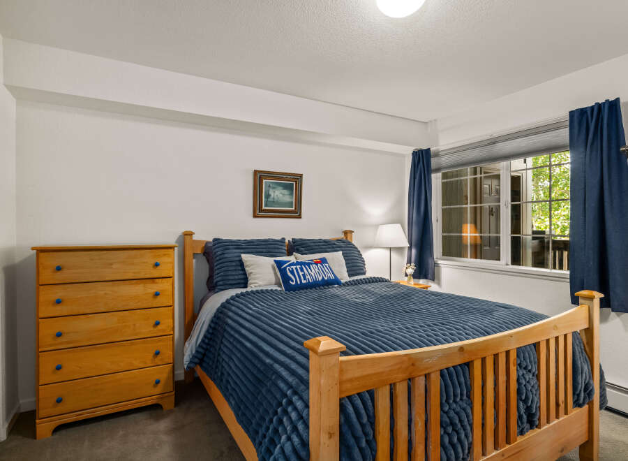 This charming bedroom features a comfortable queen-size bed with plush blue bedding, complemented by a wooden dresser with vibrant blue knobs.