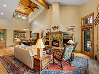 Experience rustic elegance in this spacious living room, featuring a grand stone fireplace and soaring vaulted ceilings with exposed wooden beams.