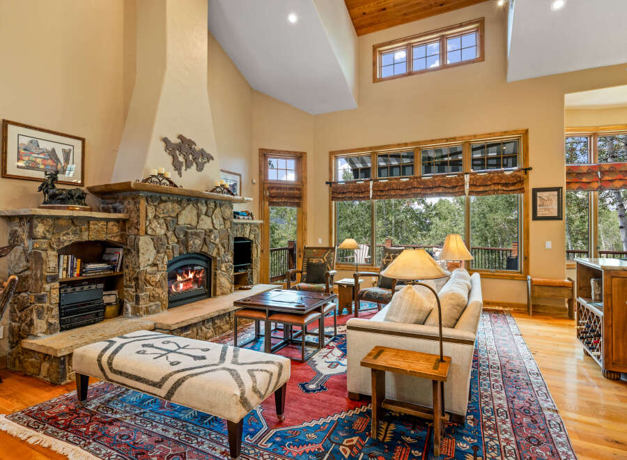 Experience rustic elegance in this spacious living room, featuring a grand stone fireplace and soaring vaulted ceilings with exposed wood beams.