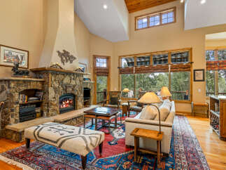 Experience rustic elegance in this spacious living room, featuring a grand stone fireplace and soaring vaulted ceilings with exposed wood beams.
