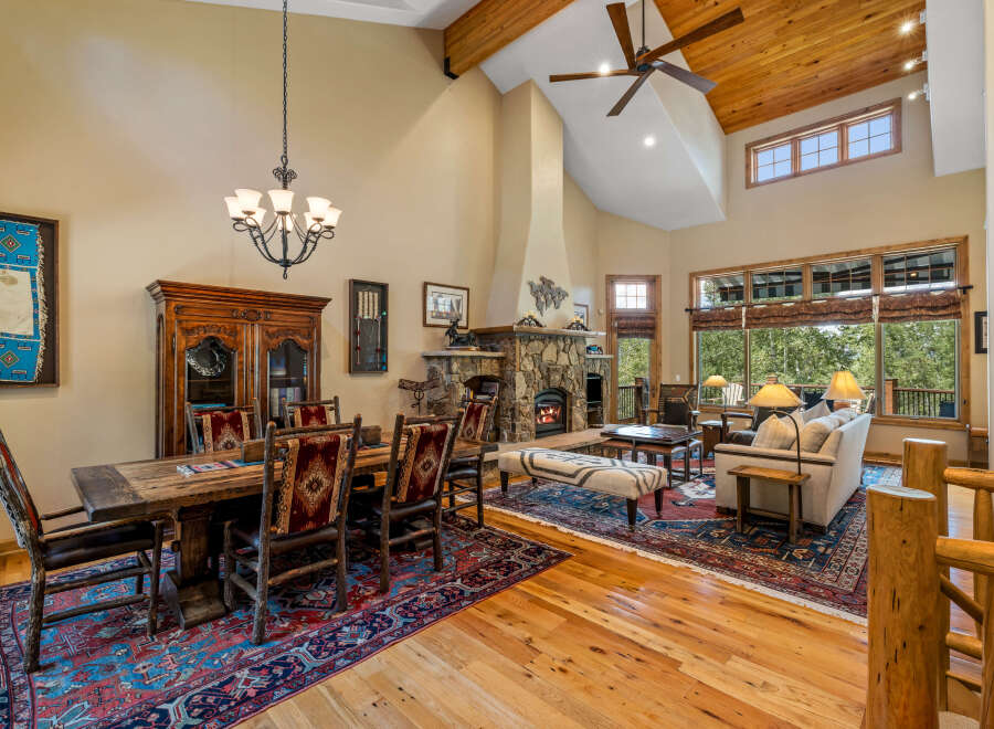 Experience rustic elegance in this spacious living and dining area, featuring a grand stone fireplace and soaring vaulted ceilings with exposed wooden beams.