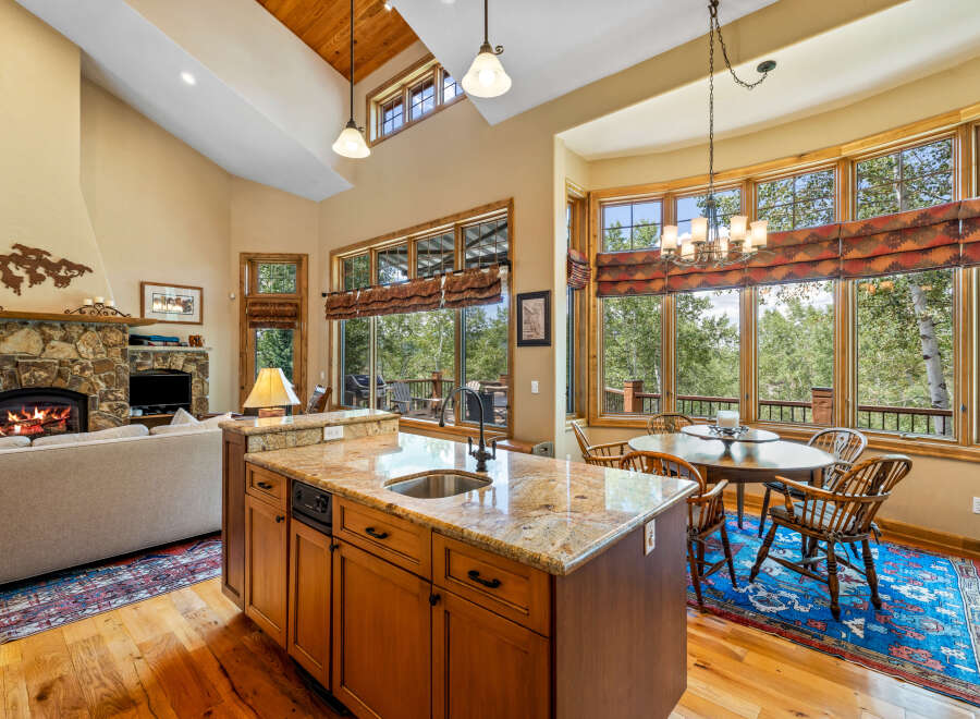Experience luxurious mountain living in this stunning open-concept kitchen and living area, featuring a grand stone fireplace and vaulted wood-paneled ceilings.