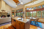 Experience luxurious mountain living in this stunning open-concept kitchen and living area, featuring a grand stone fireplace and vaulted wood-paneled ceilings.