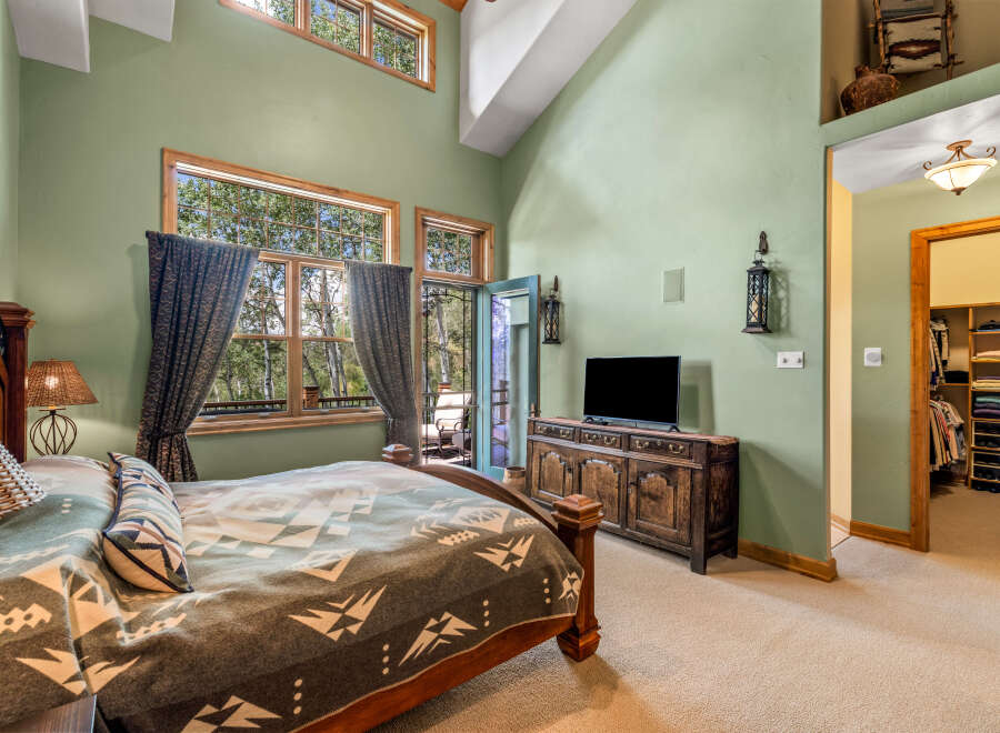 Experience luxurious living in this master bedroom featuring a vaulted ceiling and large windows that offer stunning views of the surrounding nature.