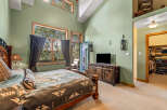Experience luxurious living in this master bedroom featuring a vaulted ceiling and large windows that offer stunning views of the surrounding nature.