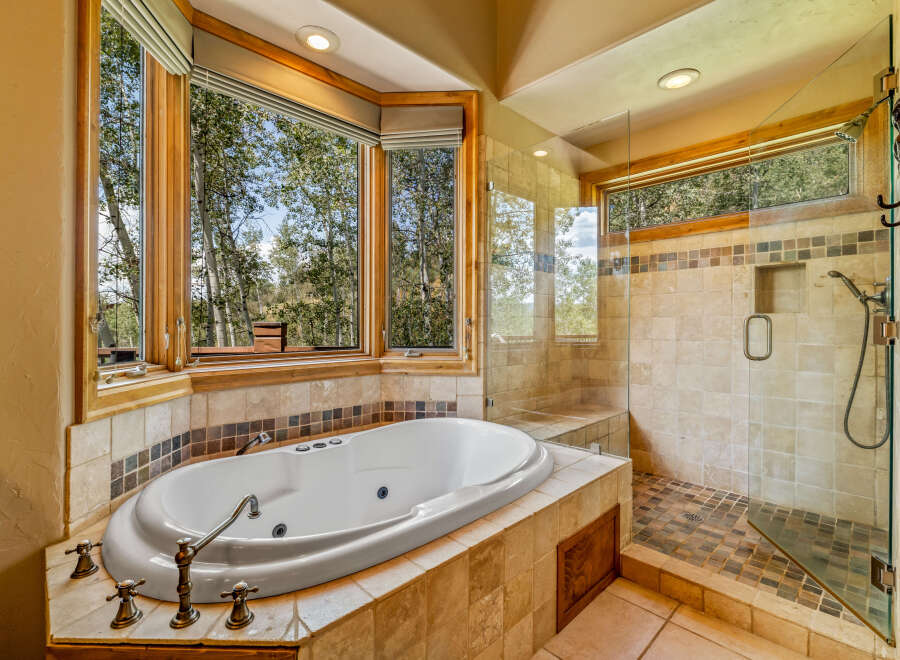 Indulge in relaxation in this luxurious bathroom featuring a spacious corner soaking tub with stunning views of the surrounding trees.