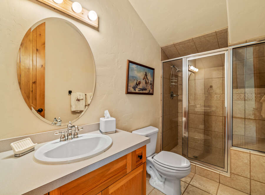 This charming bathroom features a spacious vanity with a white sink and elegant chrome fixtures, complemented by a large oval mirror with a rustic wooden frame.