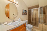 This charming bathroom features a spacious vanity with a white sink and elegant chrome fixtures, complemented by a large oval mirror with a rustic wooden frame.