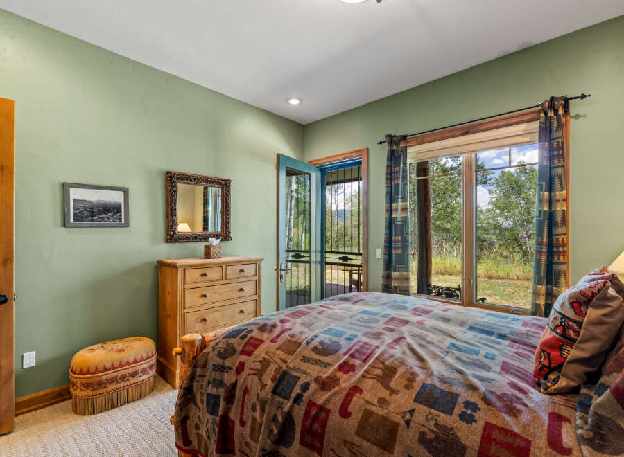 Experience rustic charm in this cozy bedroom featuring a comfortable bed with a nature-themed comforter and a decorative ottoman.