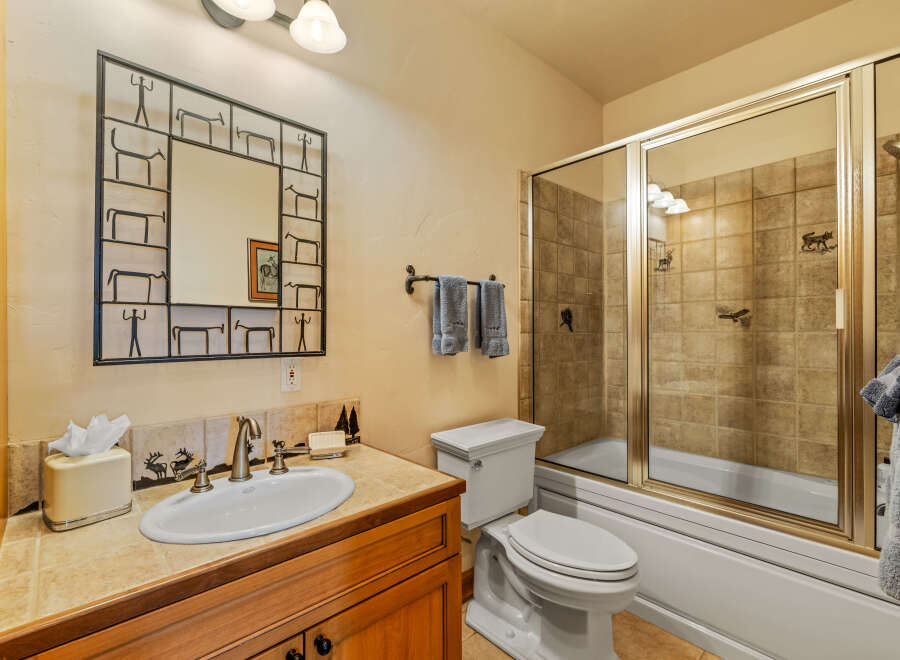This charming bathroom features a wood vanity with a tiled countertop and a white porcelain sink.