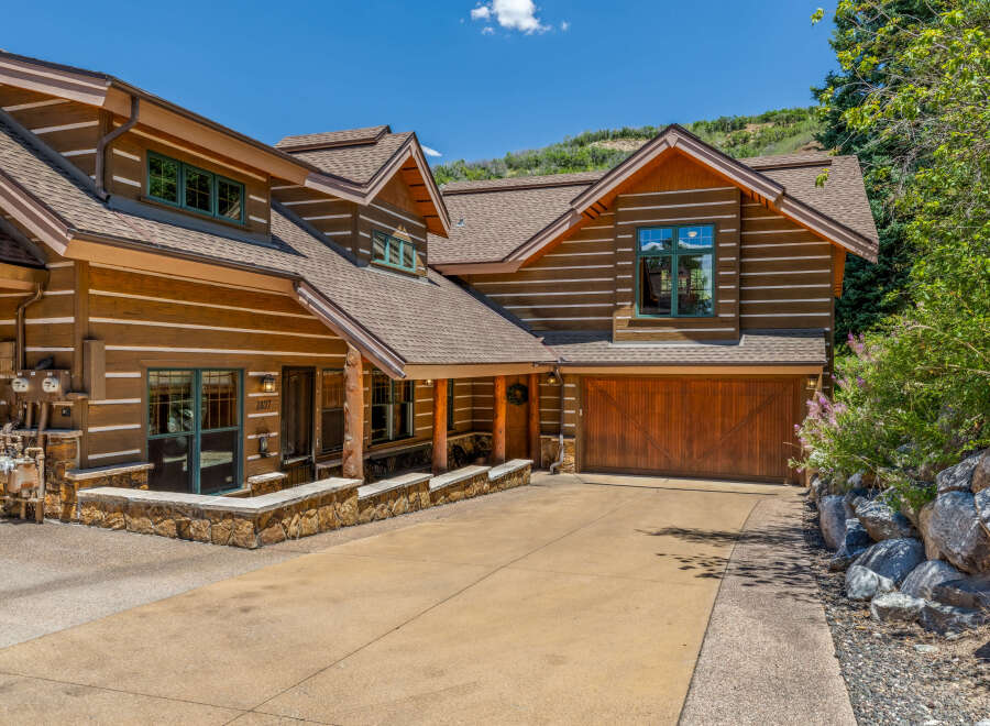 Experience rustic charm in this stunning log home, featuring a welcoming covered porch and a spacious attached garage with a beautiful wooden door.