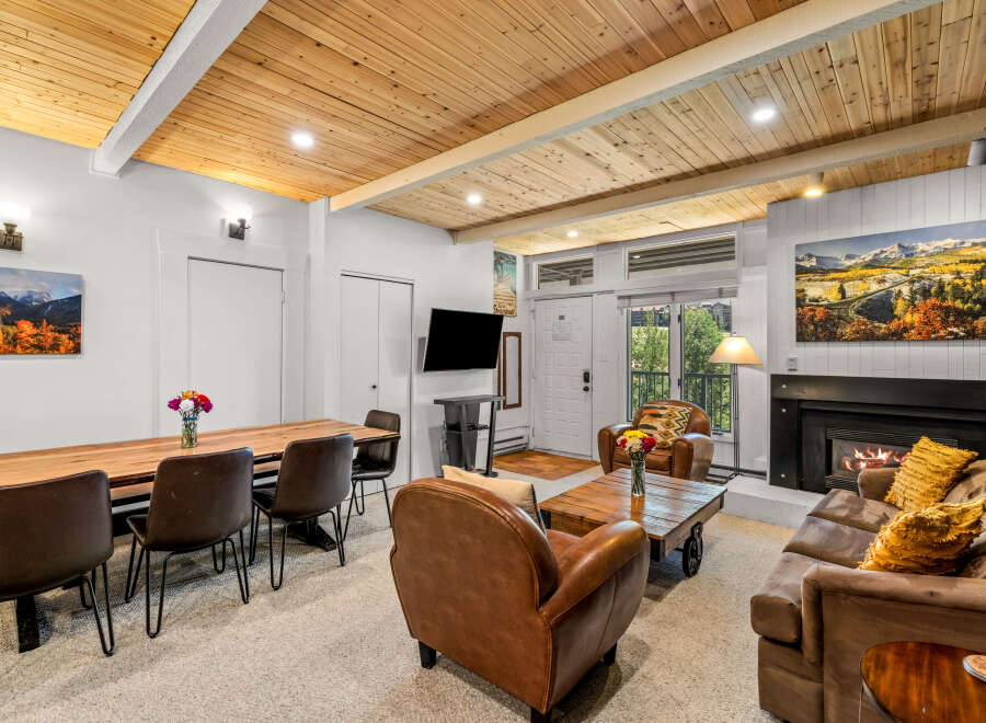 Experience cozy mountain living in this inviting living space featuring a warm fireplace and a rustic wooden dining table perfect for family gatherings.