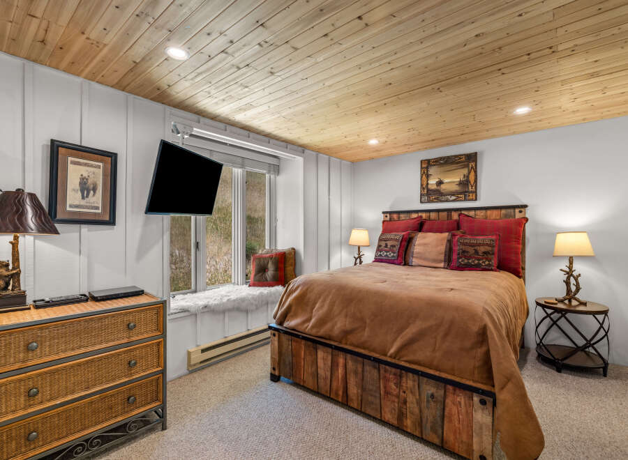 Experience rustic charm in this cozy bedroom, featuring a unique wooden bed frame and a plush window seat overlooking the natural landscape.