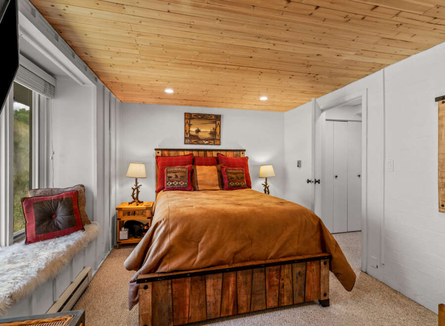 Experience rustic charm in this cozy bedroom featuring a plush queen-sized bed with a warm, inviting comforter and decorative pillows.
