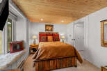 Experience rustic charm in this cozy bedroom featuring a plush queen-sized bed with a warm, inviting comforter and decorative pillows.