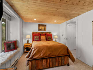 Experience rustic charm in this cozy bedroom featuring a plush queen-sized bed with a warm, inviting comforter and decorative pillows.