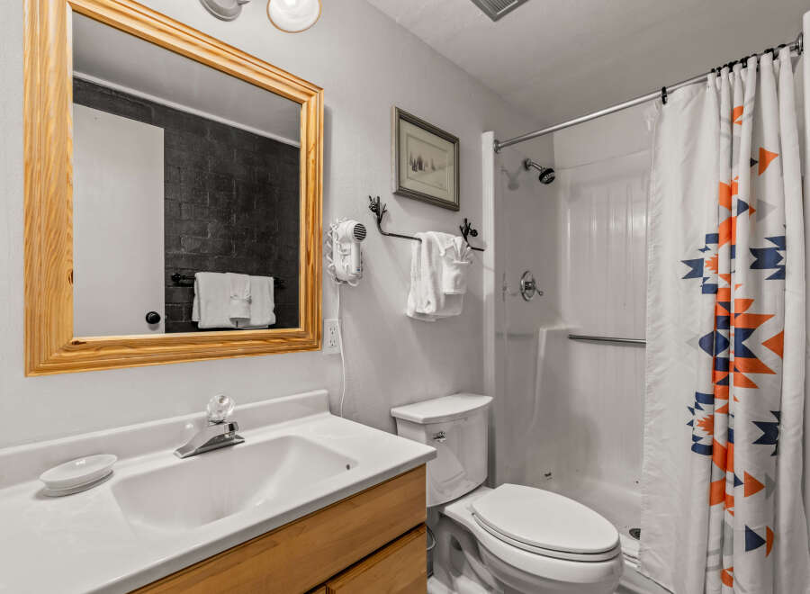 This charming bathroom features a clean white vanity with a wooden cabinet base, complemented by a large wooden-framed mirror.