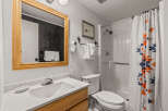 This charming bathroom features a clean white vanity with a wooden cabinet base, complemented by a large wooden-framed mirror.