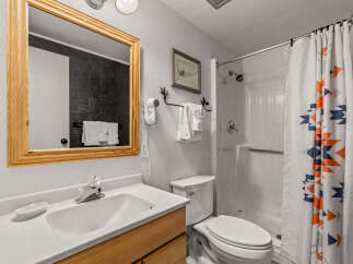 This charming bathroom features a clean white vanity with a wooden cabinet base, complemented by a large wooden-framed mirror.