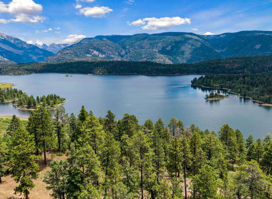 Experience breathtaking natural beauty with this stunning aerial view of a serene lake nestled amidst lush green forests and majestic mountains.