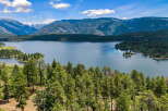 Experience breathtaking natural beauty with this stunning aerial view of a serene lake nestled amidst lush green forests and majestic mountains.