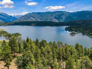 Experience breathtaking natural beauty with this stunning aerial view of a serene lake nestled amidst lush green forests and majestic mountains.
