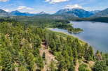 Discover breathtaking natural beauty with this stunning aerial view of a serene lake nestled amidst lush green forests and majestic mountains.