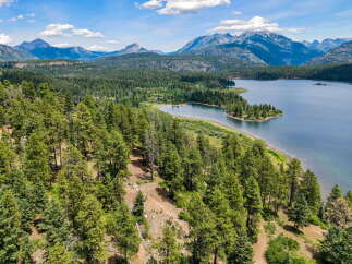 Discover breathtaking natural beauty with this stunning aerial view of a serene lake nestled amidst lush green forests and majestic mountains.