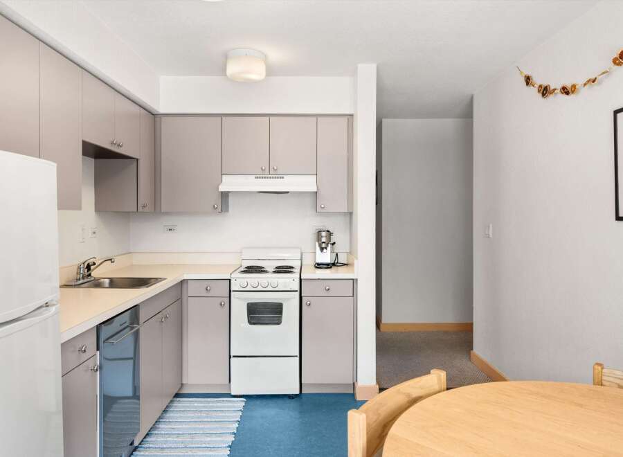 This charming kitchen features a full-size refrigerator, a stainless steel dishwasher, and a white electric range with a four-burner stovetop.