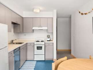 This charming kitchen features a full-size refrigerator, a stainless steel dishwasher, and a white electric range with a four-burner stovetop.