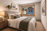 Experience cozy mountain living in this charming bedroom, featuring a plush upholstered headboard and a comfortable bed adorned with textured linens and a warm throw blanket.