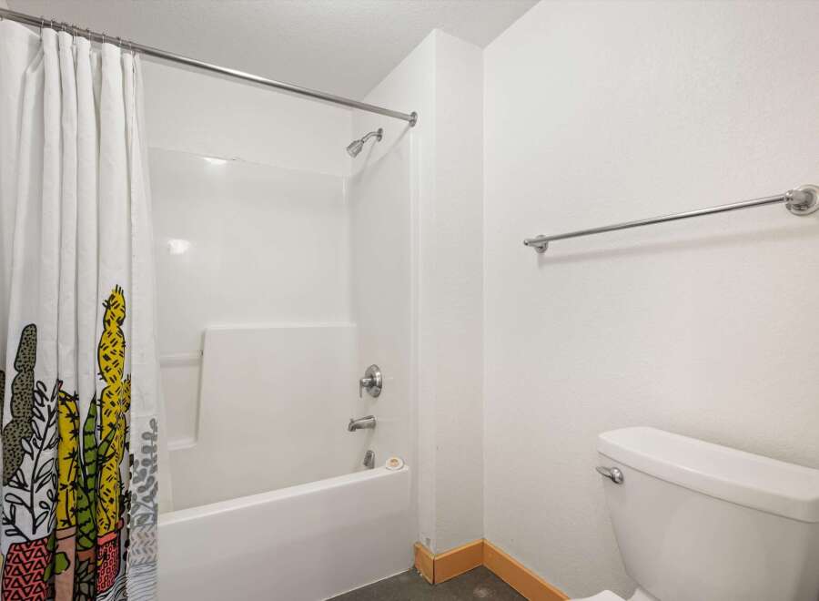 This bathroom features a clean white bathtub and shower combo, complemented by a stylish shower curtain with a cactus print.