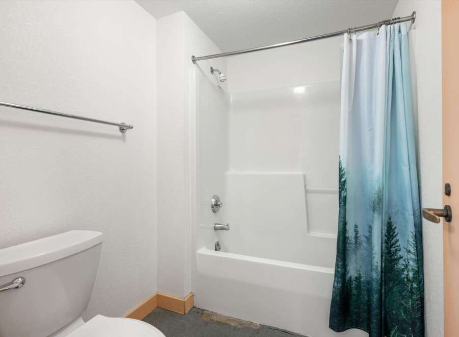 This bathroom features a clean white bathtub and shower combo, complemented by a stylish shower curtain with a forest motif.