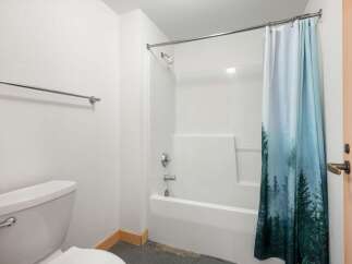 This bathroom features a clean white bathtub and shower combo, complemented by a stylish shower curtain with a forest motif.